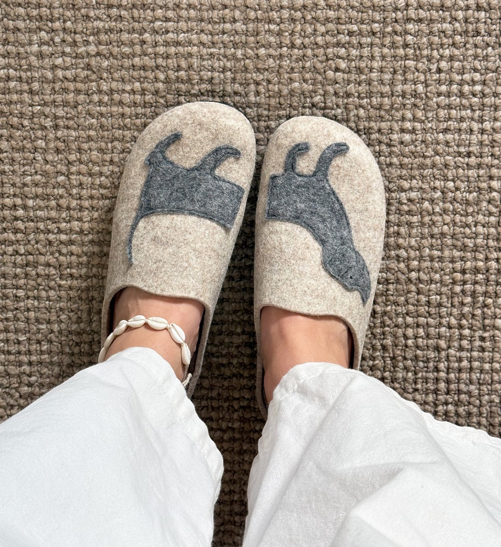House of Florian Dash slippers in beige felt with a grey dog silhouette design worn on feet with white trousers