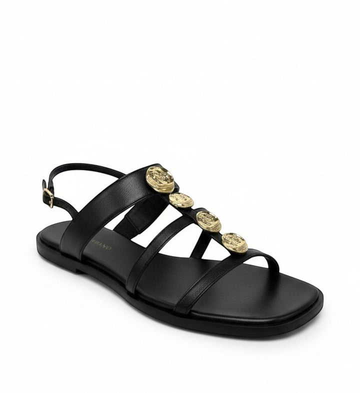 House of Florian black leather flat sandals with gold coin embellishments and adjustable ankle strap.