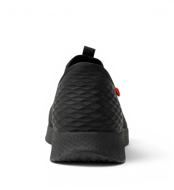 House of Florian black slip-on shoe with textured upper and rubber sole. Features a pull tab and orange accent.