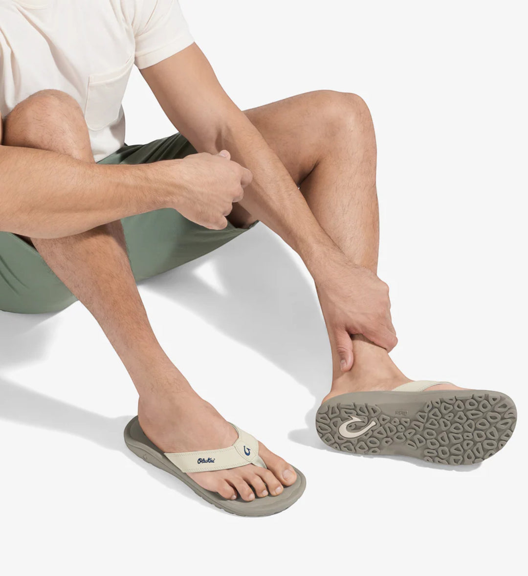 House of Florian Ohana Mens Tapa Clay flip-flops with tan straps and grey soles. A man sits wearing them.