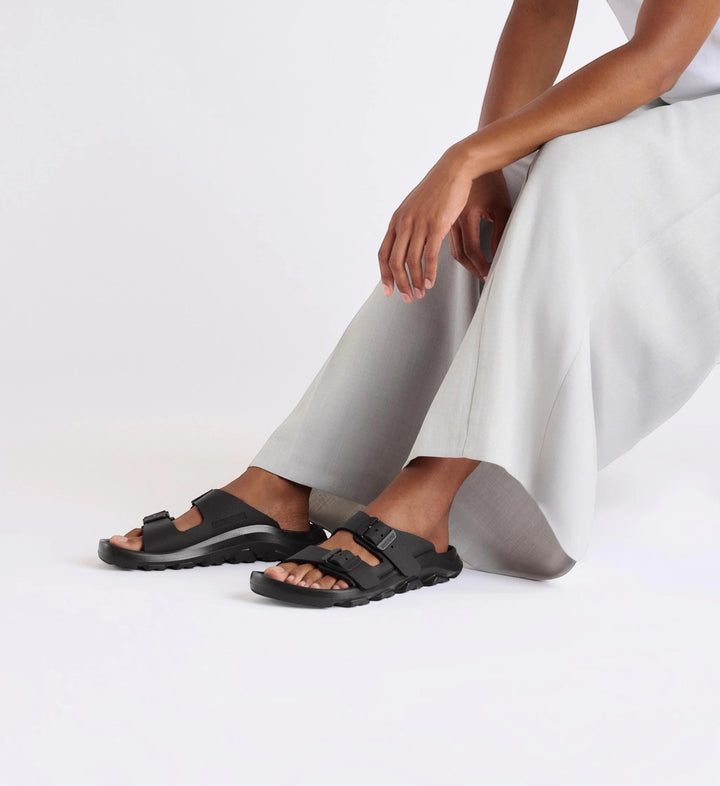 House of Florian Mogami Terra black Birko-Flor two-strap sandals worn by a model in light grey trousers